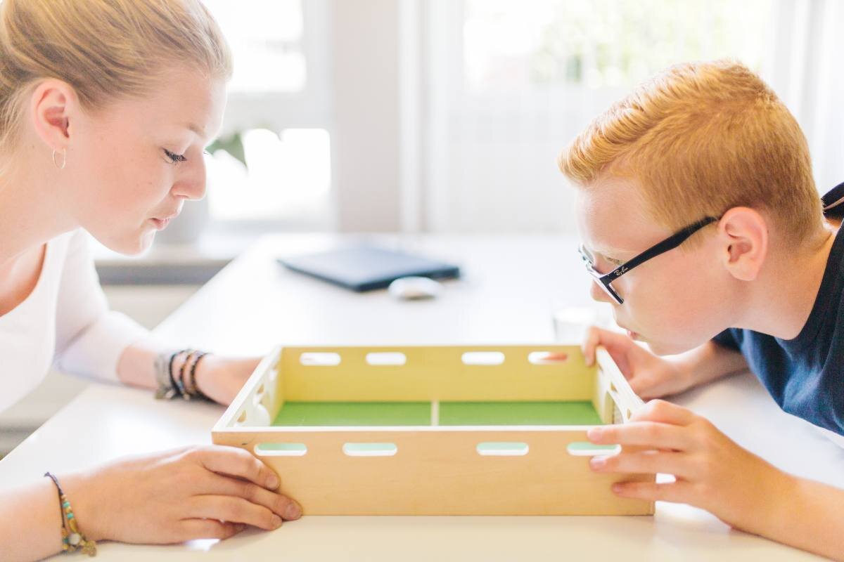 Logopädin und Kind üben konzentriert am Therapietisch mit geeignetem Übungsmaterial