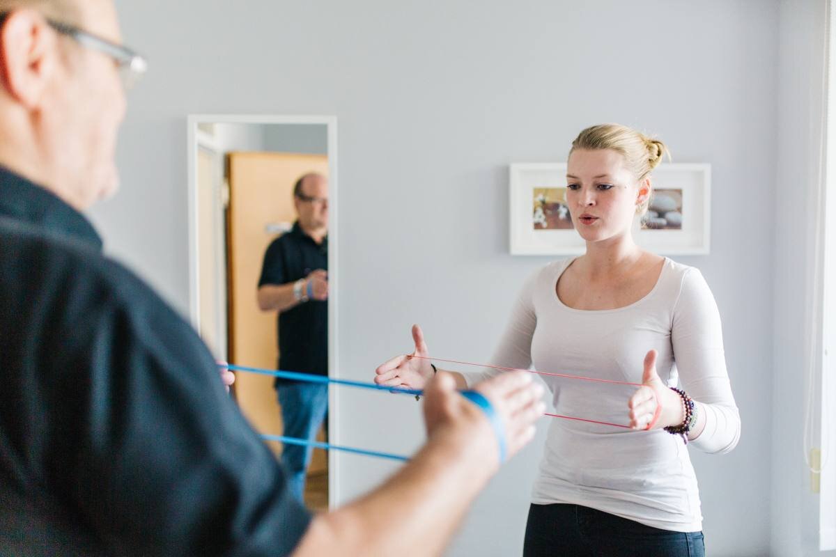 Patient trainiert Atemmuskulatur und Stimmkraft mit einem Therapieband gemeinsam mit der Logopädin