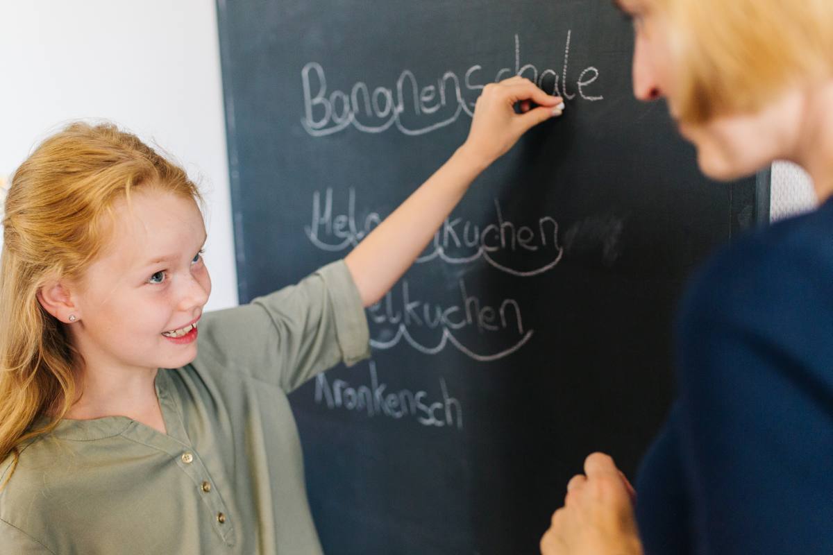 Kind schreibt Wörter an die Tafel, Therapeutin begleitet die logopädische Übung